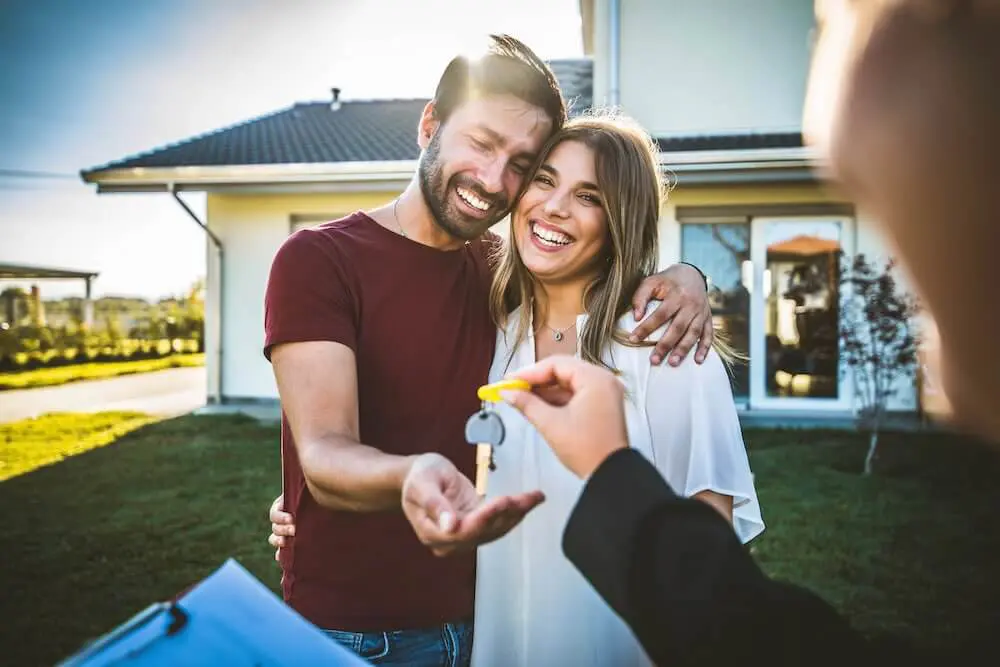 Happy young couple receiving keys from realtor after purchasing house