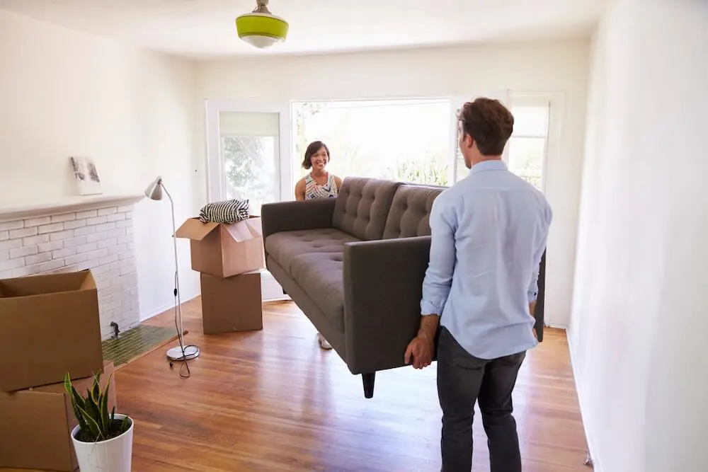 couple carrying couch into new smaller house on move in day
