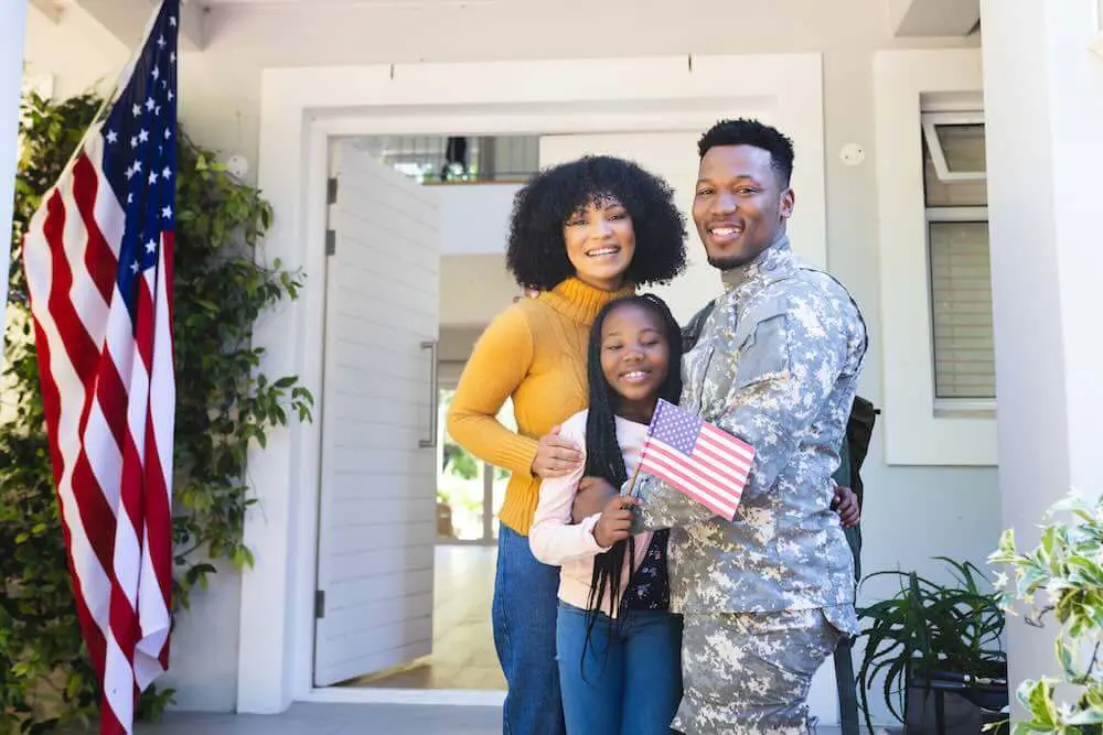 happy african american family embracing outside home with usa flag after relocating