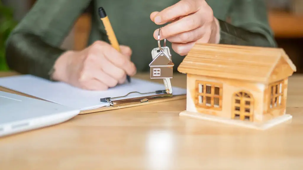 First-time buyer signing mortgage pre-approval paperwork while holding house keys at a desk.